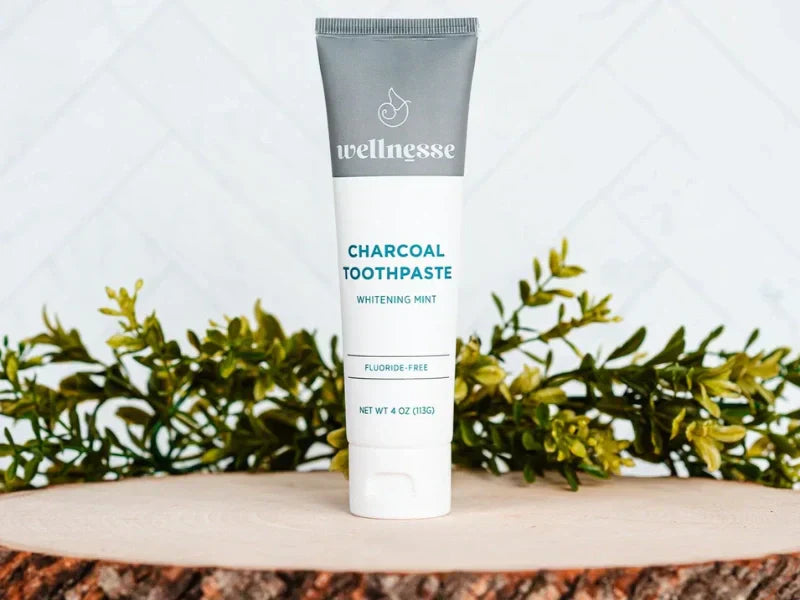 Charcoal toothpaste in whitening mint flavor showcased upright with leafy decor on a wood slab platform