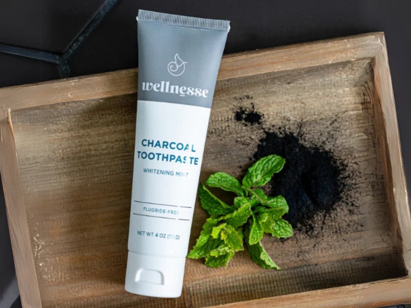 Remineralizing toothpaste with hydroxyapatite and charcoal displayed with mint and powder on wood tray.