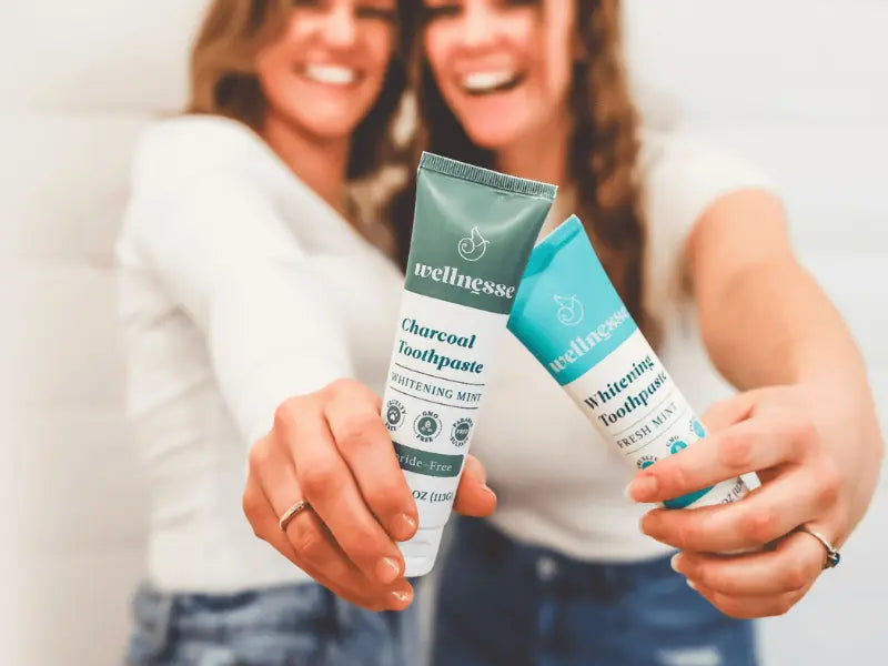 Toothpaste for sensitive teeth held by two smiling women showing fluoride-free whitening and charcoal formulas.