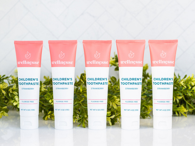 Strawberry healthy natural toothpaste in five fluoride-free tubes lined up with green foliage on a reflective white surface