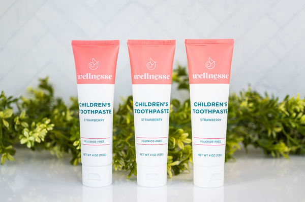 Strawberry healthy natural toothpaste in three fluoride-free tubes displayed in front of green leaves on a white surface
