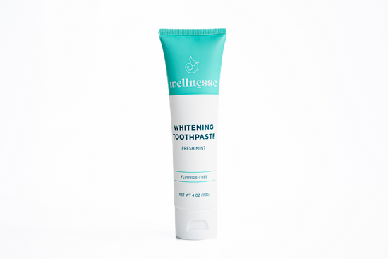 Natural teeth whitening toothpaste in a Wellnesse tube with a turquoise top and white body, labeled fluoride-free fresh mint.