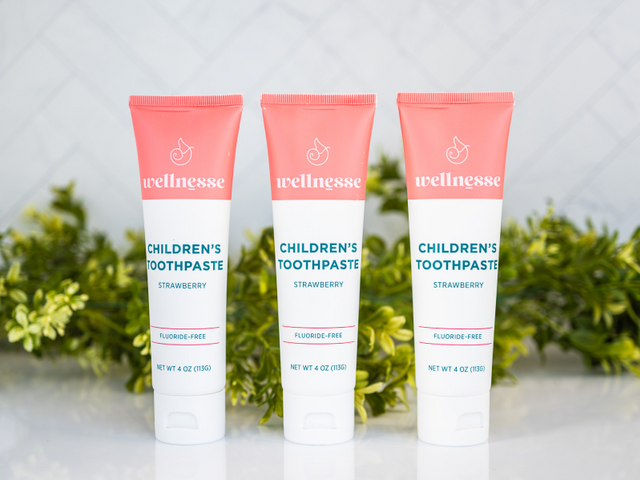 Strawberry healthy natural toothpaste in three fluoride-free tubes displayed in front of green leaves on a white surface