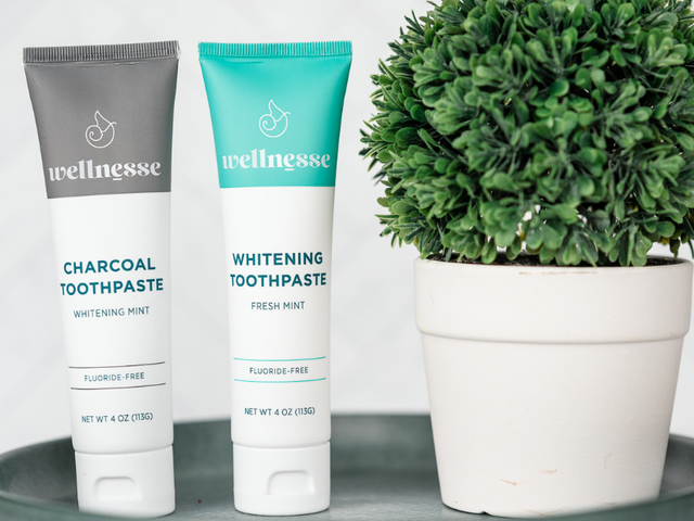 Charcoal and mint organic hydroxyapatite toothpaste tubes displayed alongside bamboo toothbrushes and natural dental floss on a wooden tray