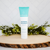 Fluoride free whitening toothpaste displayed on a wooden slab with greenery, featuring a Wellnesse fresh mint tube.