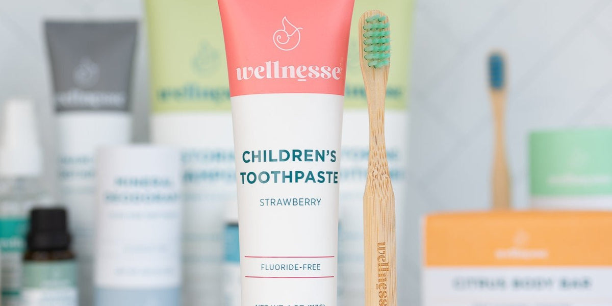 Strawberry natural ingredient toothpaste for children by Wellnesse, shown with a bamboo toothbrush and natural personal care products in the background.