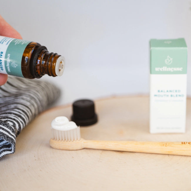 Concentrated mouthwash being applied to toothpaste on a bamboo toothbrush next to Wellnesse Balanced Mouth Blend box.