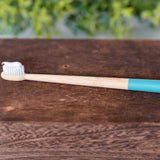 Bamboo toothbrush with blue handle tip and toothpaste on bristles resting on a dark wooden box.