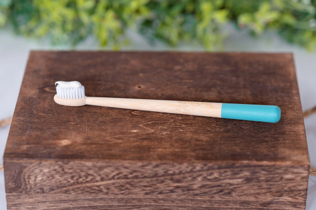 Bamboo toothbrush with blue handle tip and toothpaste on bristles resting on a dark wooden box.