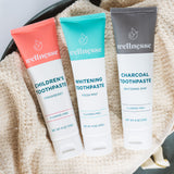 Natural chemical free toothpaste trio featuring children's strawberry, fresh mint whitening, and charcoal whitening varieties on a soft beige towel