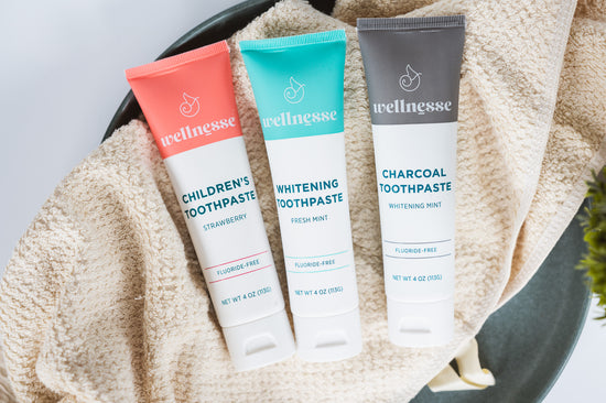 Natural chemical free toothpaste trio featuring children's strawberry, fresh mint whitening, and charcoal whitening varieties on a soft beige towel