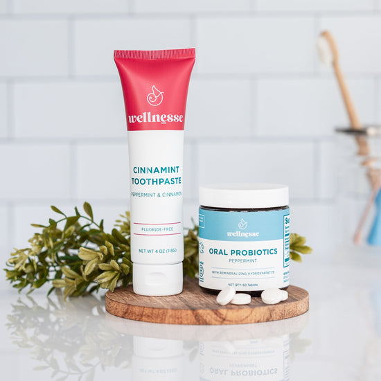 Cinnamon non toxic whitening toothpaste from Wellnesse paired with oral probiotics, displayed on a wooden tray with mint leaves.
