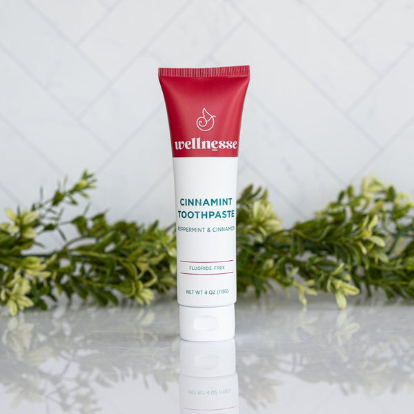 Cinnamon fluoride free toothpaste in a Wellnesse Cinnamint tube featuring peppermint and cinnamon, displayed with green foliage.