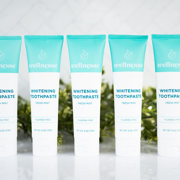 Mint whitening toothpaste five-pack from Wellnesse featuring fluoride-free fresh mint formula, displayed with a green foliage background.