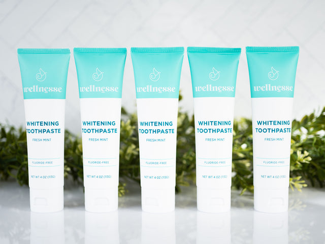 Mint whitening toothpaste five-pack from Wellnesse with fluoride-free fresh mint formula, displayed in front of lush green leaves.
