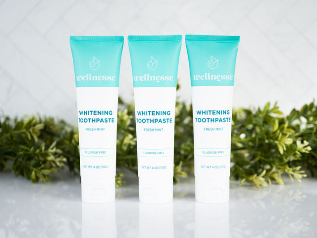 Mint whitening toothpaste trio from Wellnesse with fluoride-free formula, displayed in front of fresh greenery and a tiled backdrop.
