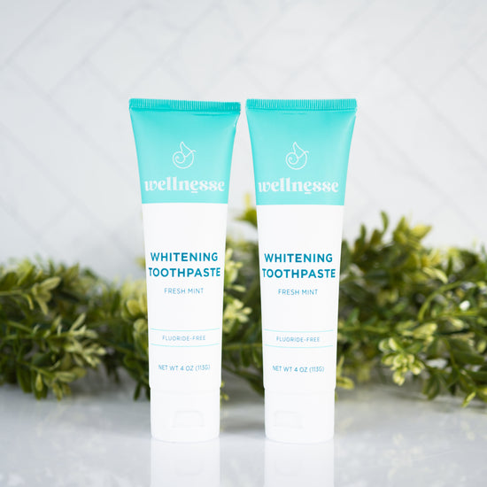 All natural whitening toothpaste tubes from Wellnesse, featuring fresh mint flavor and fluoride-free formula with green foliage background.