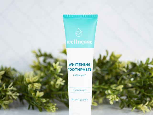 Fluoride free mint whitening toothpaste from Wellnesse in a turquoise and white tube, placed in front of lush greenery.