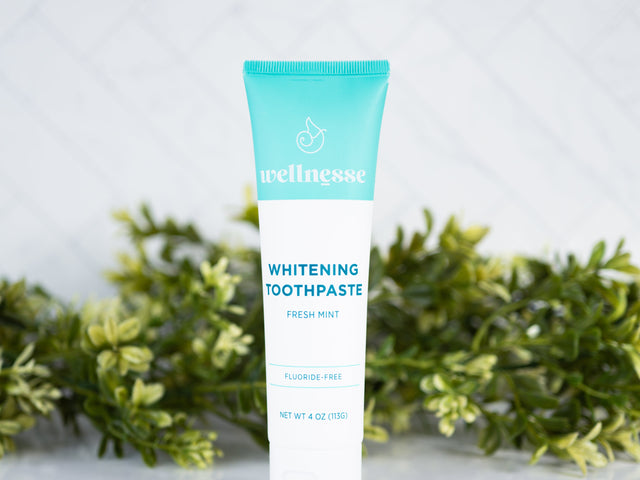 Fluoride free mint whitening toothpaste from Wellnesse displayed in front of green foliage on a tiled surface.