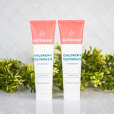 Strawberry healthy toothpaste without fluoride in two tubes displayed with green plants on a clean bathroom counter.
