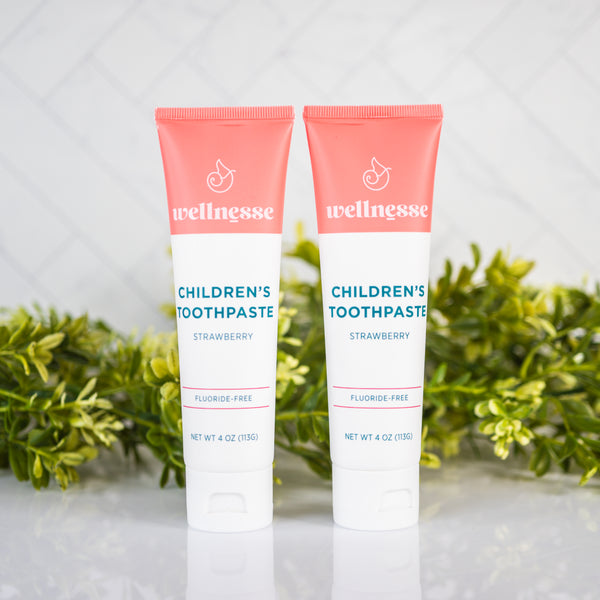 Strawberry healthy toothpaste without fluoride in two tubes displayed with green plants on a clean bathroom counter.