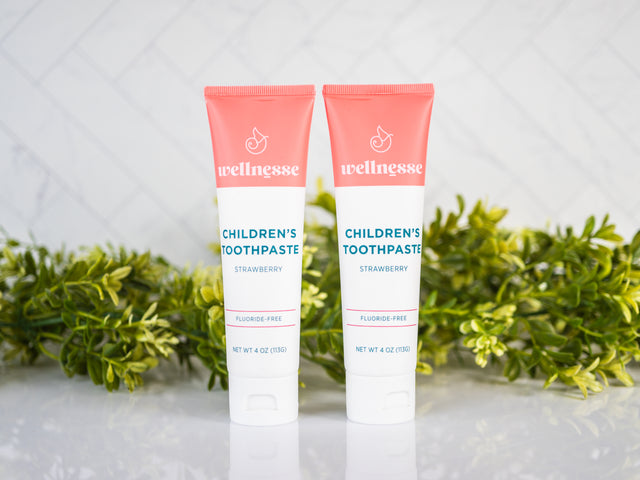 Strawberry healthy toothpaste without fluoride in two tubes displayed with green plants on a clean bathroom counter.
