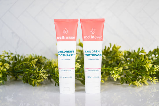 Strawberry healthy toothpaste without fluoride in two tubes displayed with green plants on a clean bathroom counter.