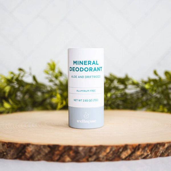 Aluminum free deodorant labeled Mineral Deodorant with aloe and driftwood scent, displayed on a wooden slice with greenery.