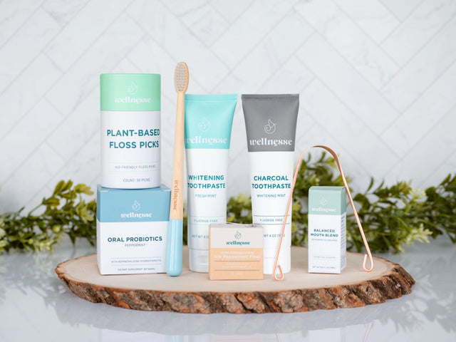 Oral care kit featuring Wellnesse products including toothpaste, floss, probiotics, floss picks, mouth blend, toothbrush, and tongue scraper.