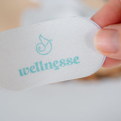 White mouth tape with 'wellnesse' branding held by a hand on a light background