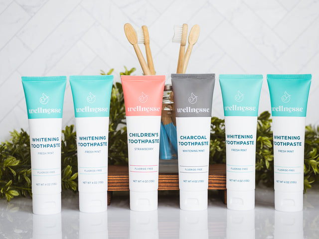 Organic hydroxyapatite toothpaste lineup including whitening mint, charcoal, and children's strawberry flavors with bamboo toothbrushes in a glass jar