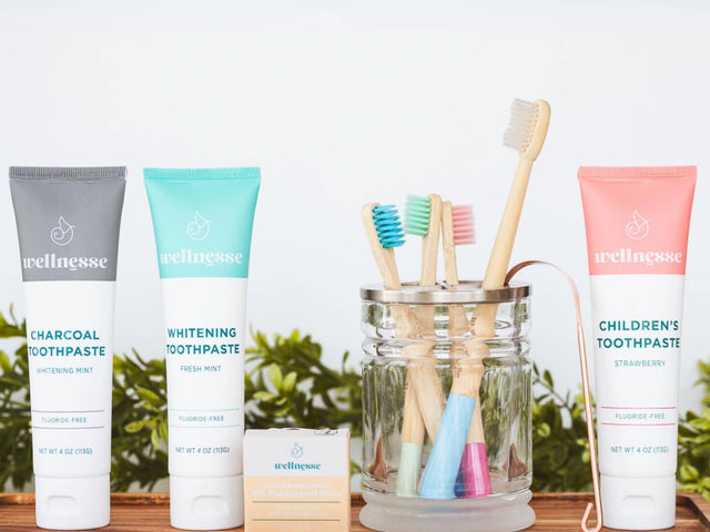 Organic hydroxyapatite toothpaste varieties including strawberry, charcoal, and mint displayed with bamboo toothbrushes and floss on a tray