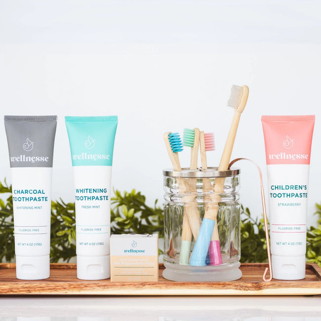 Organic hydroxyapatite toothpaste varieties including strawberry, charcoal, and mint displayed with bamboo toothbrushes and floss on a tray