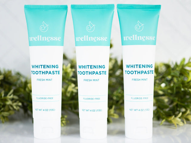 Best all natural whitening toothpaste trio from Wellnesse in fresh mint flavor, fluoride-free formula, displayed with green foliage backdrop.