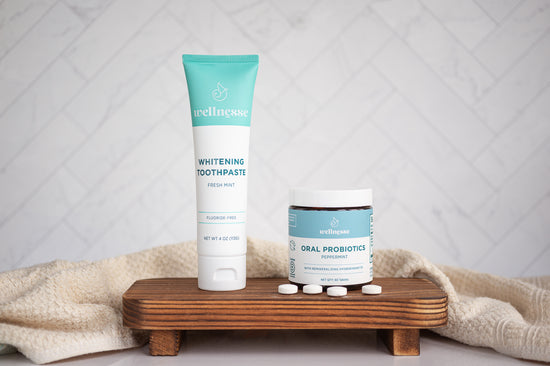 Oral probiotics in peppermint flavor by Wellnesse shown beside whitening toothpaste on a wooden stand with tablets scattered.