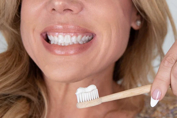 Smiling person holding a bamboo toothbrush with a stripe of natural whitening toothpaste.