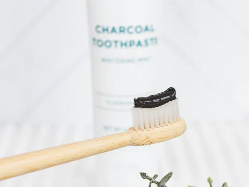 Best charcoal toothpaste applied to a bamboo toothbrush with product tube softly blurred in the background.
