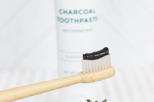 Best charcoal toothpaste applied to a bamboo toothbrush with product tube softly blurred in the background.