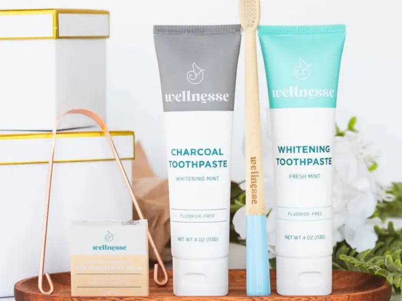 Calcium phosphate toothpaste in charcoal and mint varieties with bamboo toothbrush and floss on a wooden tray.