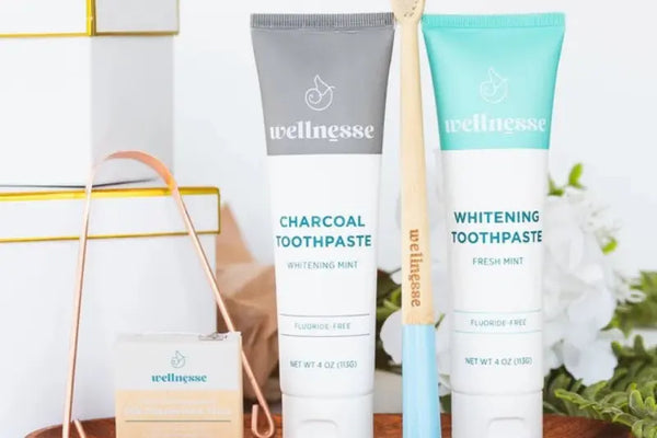 Calcium phosphate toothpaste in charcoal and mint varieties with bamboo toothbrush and floss on a wooden tray.