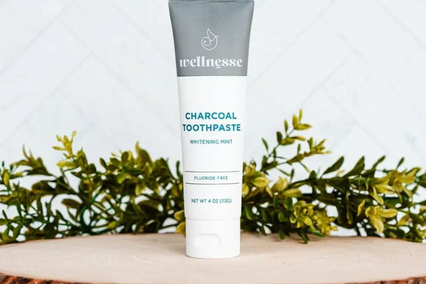 Wellnesse charcoal whitening mint toothpaste tube on a wood slice with greenery.