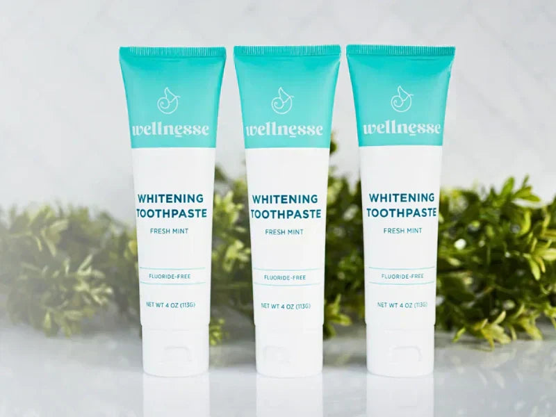 Fluoride-free toothpaste tubes standing in a row with green foliage in the background on a marble surface