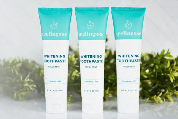 Fluoride-free toothpaste tubes standing in a row with green foliage in the background on a marble surface
