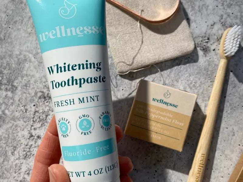 Hydroxyapatite toothpaste Wellnesse Whitening Toothpaste shown with biodegradable floss and a bamboo toothbrush.