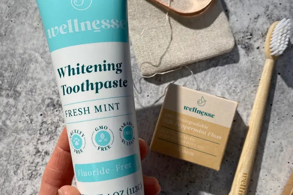 Hydroxyapatite toothpaste Wellnesse Whitening Toothpaste shown with biodegradable floss and a bamboo toothbrush.