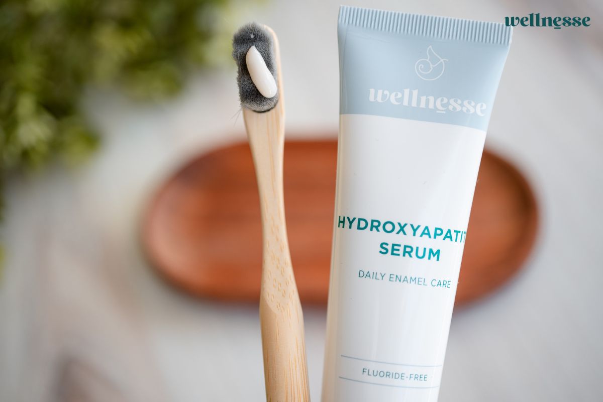 Bamboo toothbrush with a dab of hydroxyapatite serum beside a fluoride-free Wellnesse enamel serum tube.
