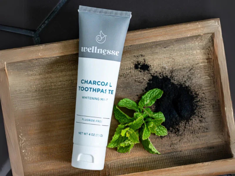 Remineralizing toothpaste with hydroxyapatite and charcoal displayed with mint and powder on wood tray.