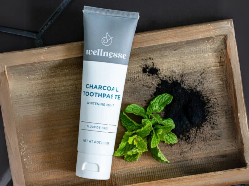 Remineralizing toothpaste with hydroxyapatite and charcoal displayed with mint and powder on wood tray.