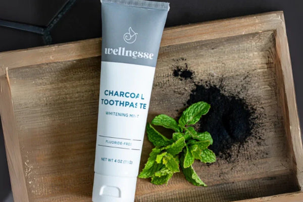 Remineralizing toothpaste with hydroxyapatite and charcoal displayed with mint and powder on wood tray.