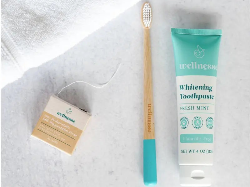 Best fluoride-free toothpaste paired with bamboo toothbrush and silk peppermint floss on white surface.